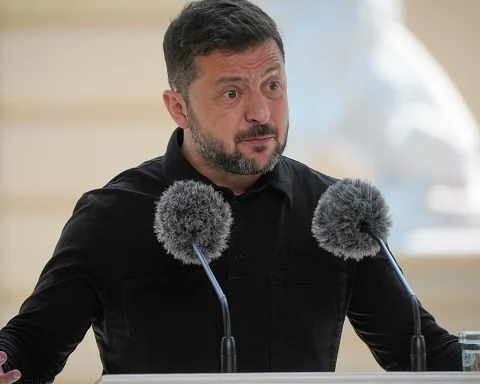 Man in a black shirt speaks at a podium with two fuzzy microphones during a press conference.