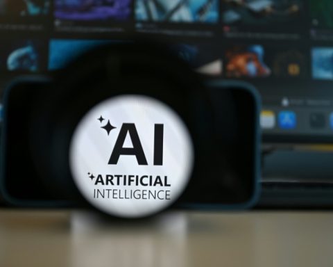 Close-up of a lens/magnifier showing the text 'AI' with sparkles and 'Artificial Intelligence' beneath it, against a blurred screen backdrop.