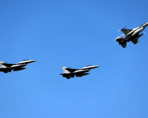 Three gray fighter jets in formation flying left to right across a clear blue sky.