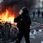 Riot police officer stands near a burning barricade during unrest in Paris